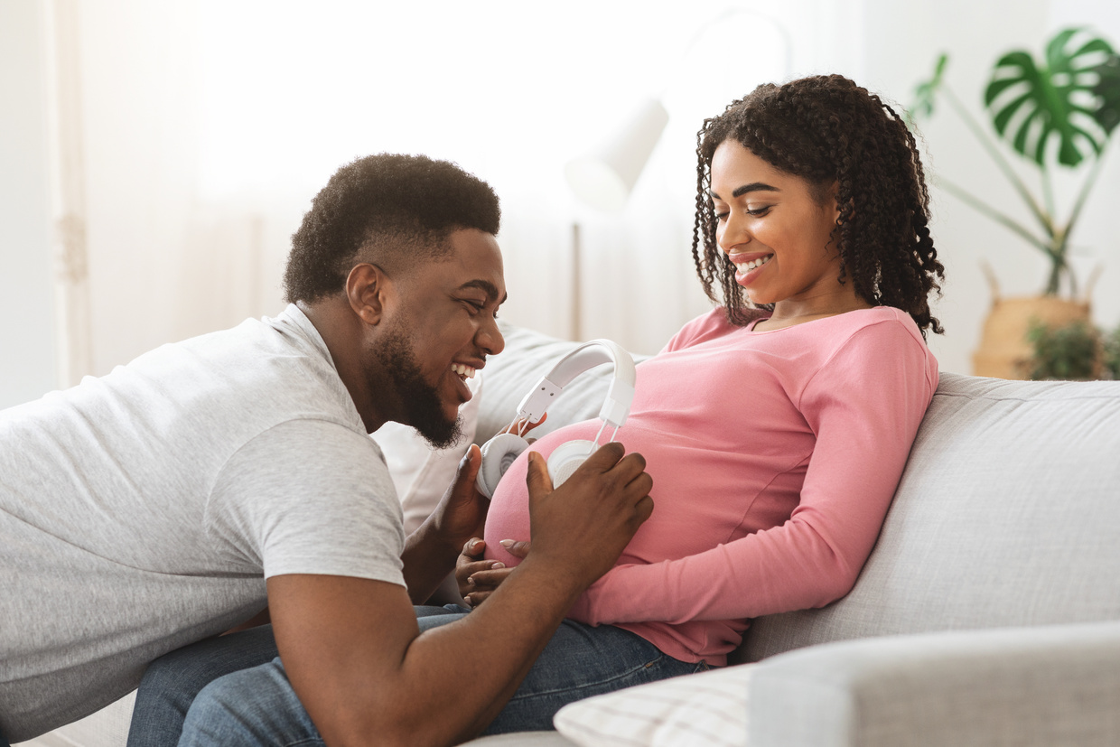 Black father holding headset on pregnant woman belly